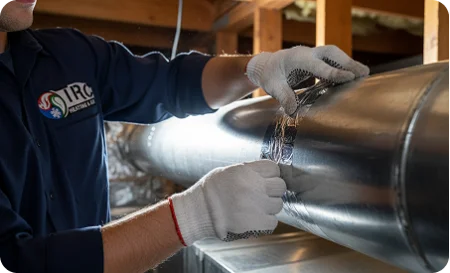 Professional technician's gloved hands applying sealant or adhesive tape to a large metal air duct