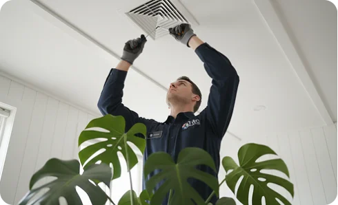 HVAC technician in blue gloves using a tool to adjust wiring on a system control board.